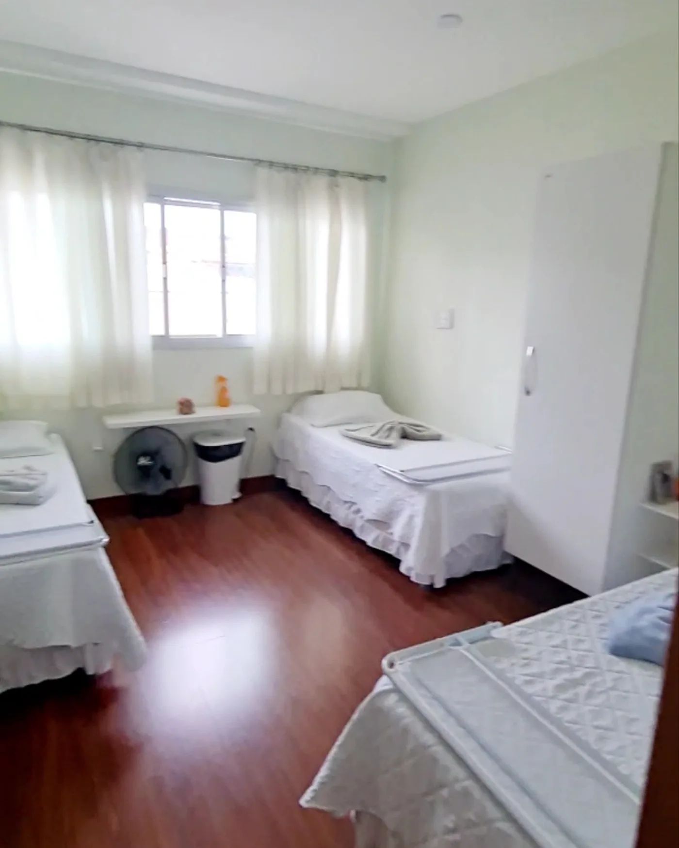 Quarto duplo da LARES, com duas camas, janela e piso de madeira