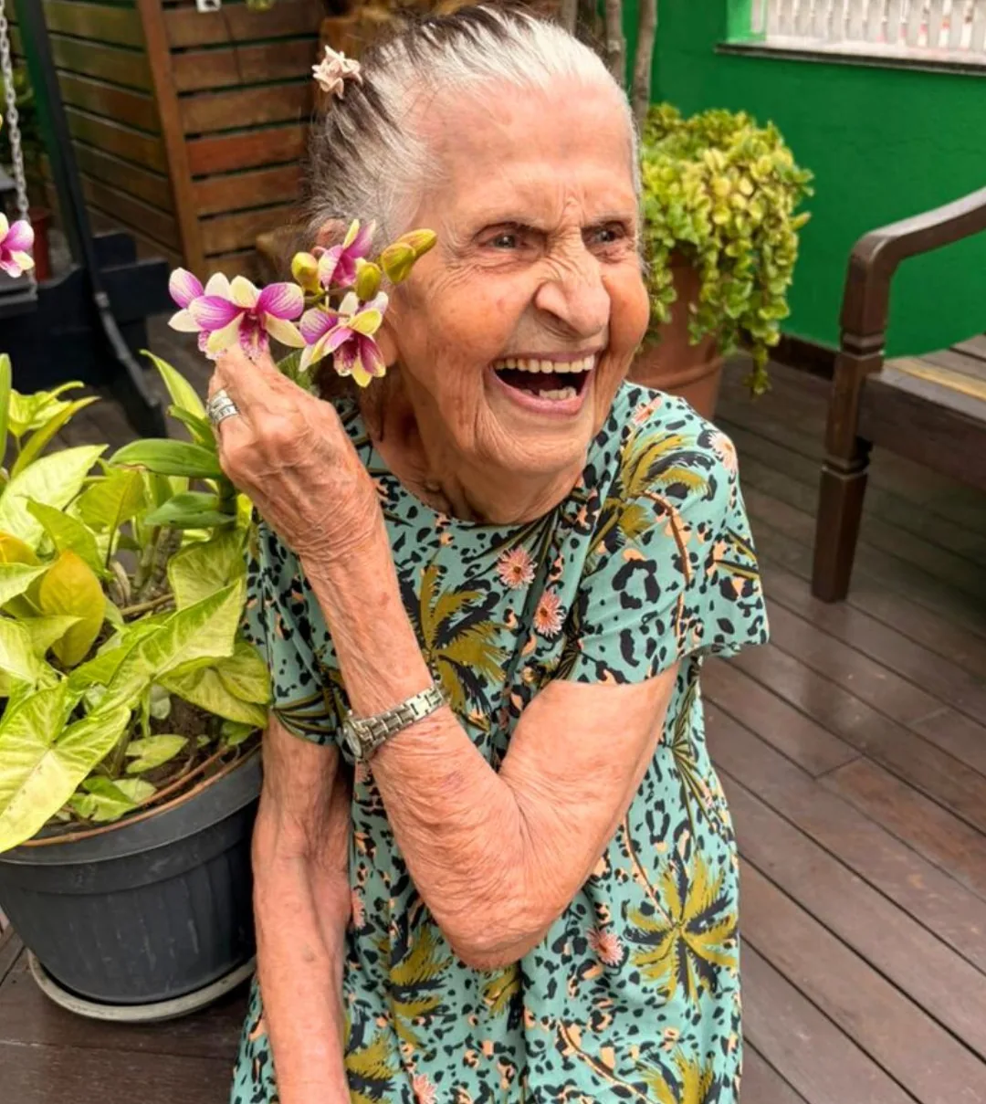 Moradora da LARES rindo no quintal, com uma orquídea na mão