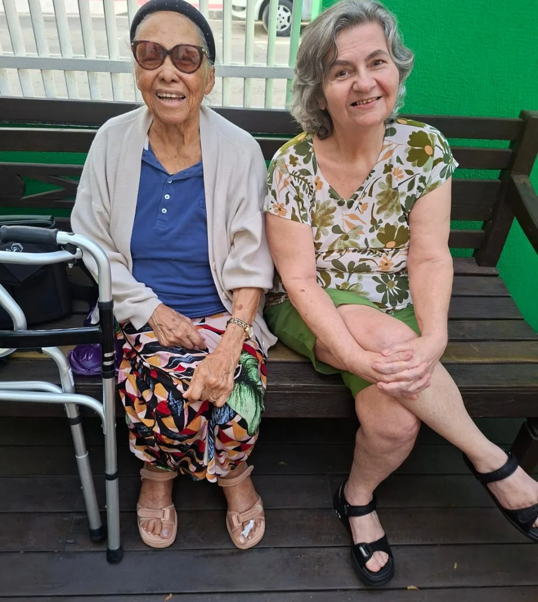 Duas moradoras da LARES sentadas juntas no banco de madeira da varanda, sorrindo