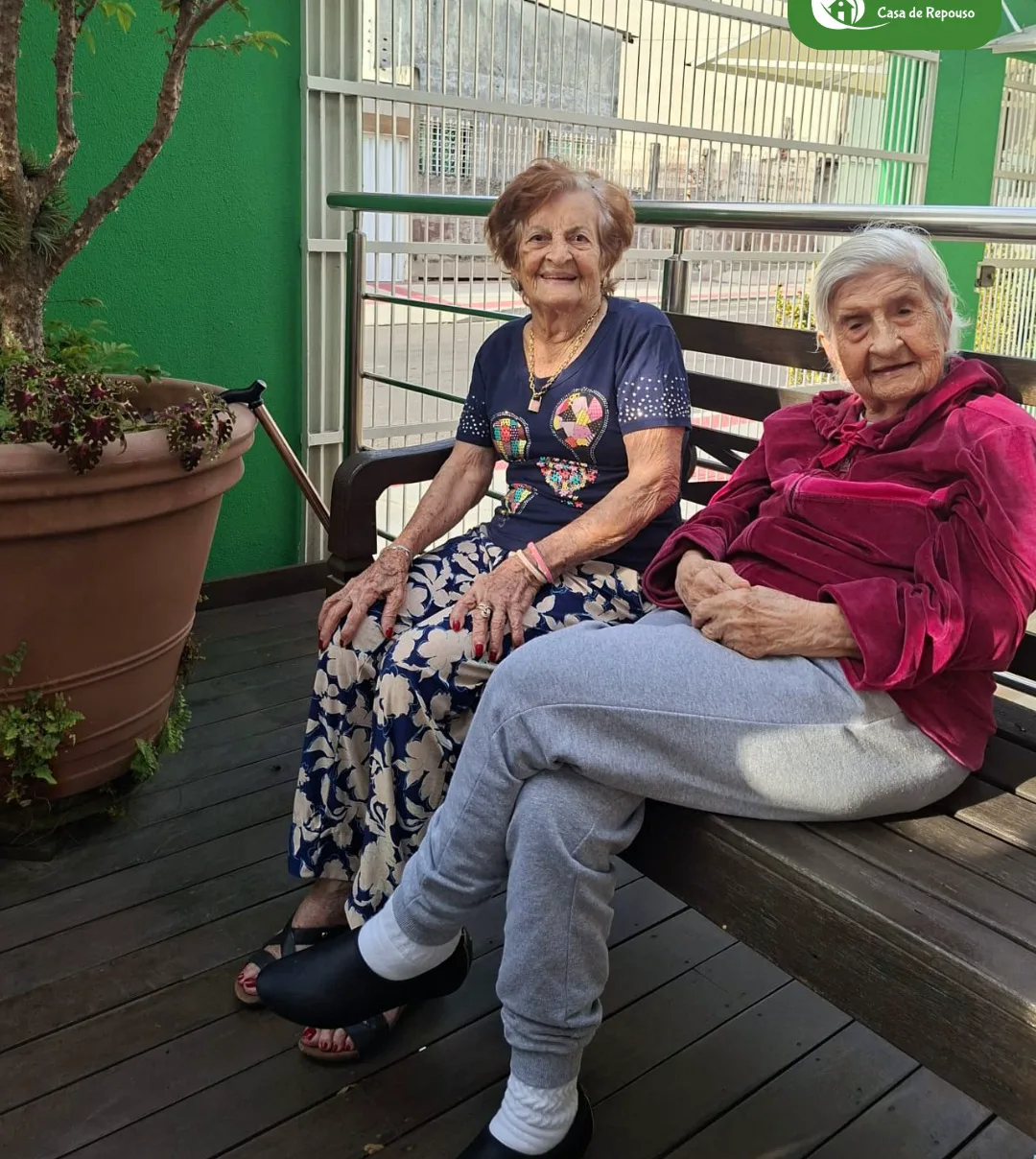 Duas moradoras da LARES sentadas lado a lado no banco da varanda, conversando